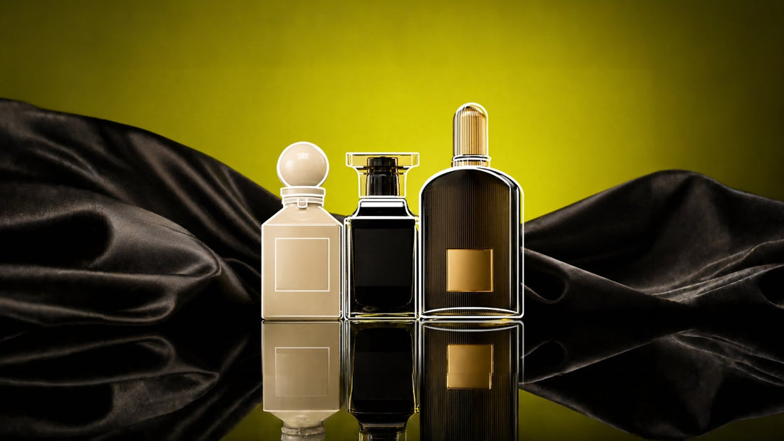 Three luxury perfume bottles—cream, black, and ribbed gold—on a reflective surface, framed by draped black satin against a glowing yellow background.