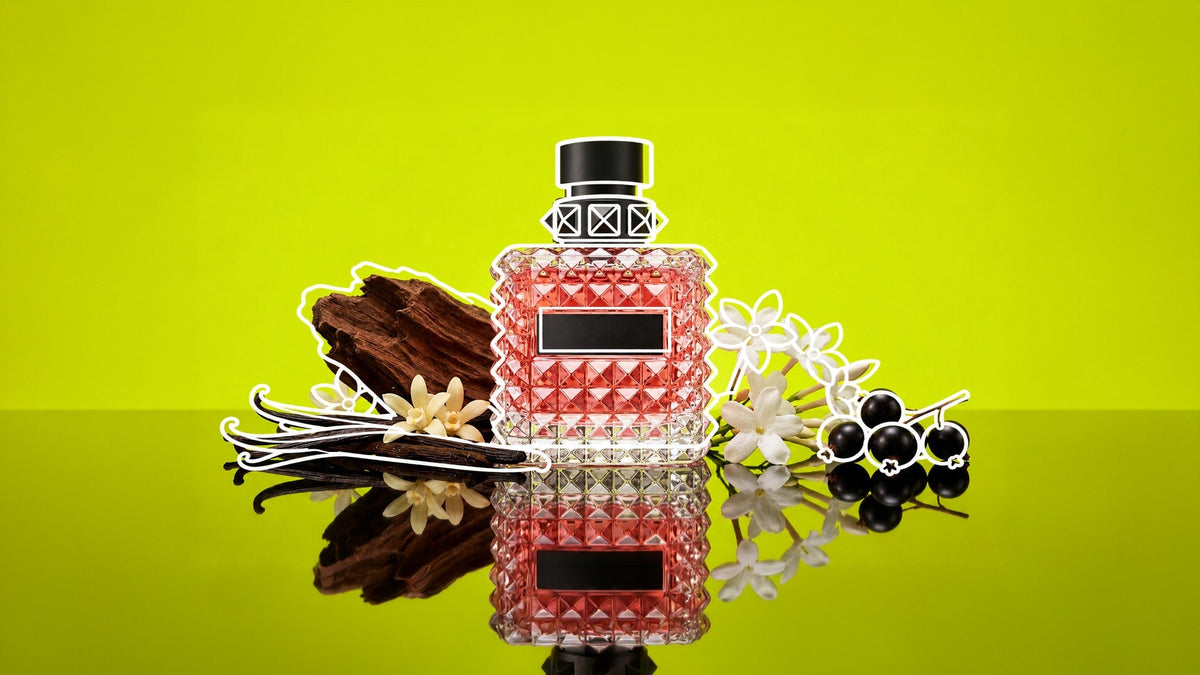 Pink perfume bottle with a textured glass design and black cap, surrounded by vanilla pods, wood, white flowers, and black berries on a reflective surface against a vibrant lime-green background.